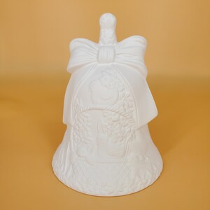 May include: White ceramic bell with a bow on top and a raised design of a snowman and holly. The bell is ready to be painted.