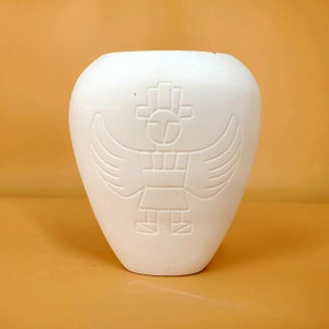 Puede incluir: Jarrón de cerámica blanco con un diseño en relieve de una figura estilizada con alas. La figura está en el centro del jarrón y tiene un diseño geométrico.