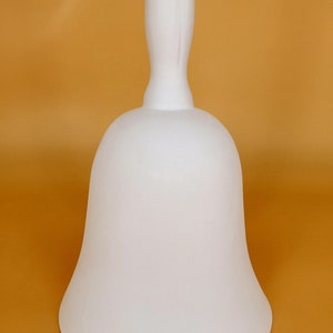 May include: A white ceramic bell with a rounded base and a tall, slender handle. The bell is smooth and has a glossy finish.