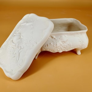 May include: White ceramic trinket box with a floral design and a lid. The box has four legs and is decorated with raised floral details.