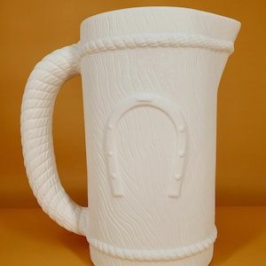 Puede incluir: Jarra de cerámica blanca con un asa de cuerda y un diseño de veta de madera. La jarra tiene un diseño de herradura en la parte delantera.