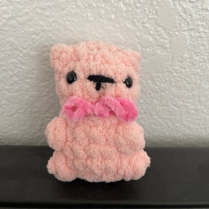 May include: A small pink crocheted teddy bear with black eyes and a pink yarn bow.