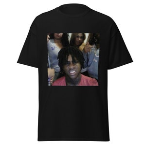 May include: A black t-shirt with a printed image of a young man with dreadlocks and a red shirt, surrounded by three women. The man is looking at the camera and has a serious expression on his face.