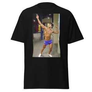 May include: A man in a locker room wearing blue athletic shorts and white sneakers. He is flexing his muscles and looking up.