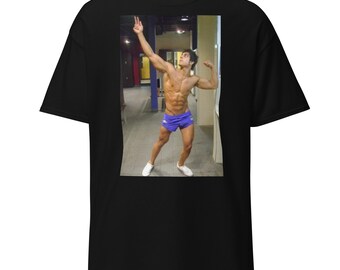 Pode incluir: Um homem em um vestiário usando shorts esportivos azuis e tênis brancos. Ele está flexionando os músculos e olhando para cima.