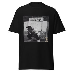 May include: Black and white photo of a man wearing a baseball cap and a t-shirt, sitting in front of a vending machine with the words "crystal clear ICE" on it. The photo is on a black t-shirt with the words "GOTHAM CITY ICE" and "RECORDS" printed on it.
