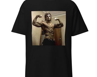 May include: A black t-shirt with a photo of a shirtless man flexing his muscles. The man has short, dark hair and is wearing black pants.