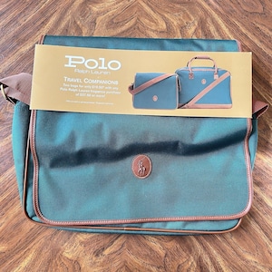 May include: A green Polo Ralph Lauren messenger bag with brown trim and a brown logo patch. The image also shows a promotional card with the text "TRAVEL COMPANIONS" and two matching bags.