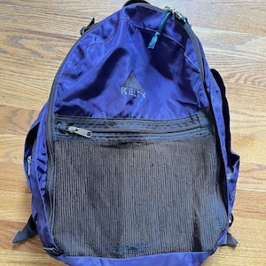 May include: A blue Kelty backpack with a black mesh pocket and a zippered compartment. The backpack has black straps and a small logo. The backpack is made of a durable material and is designed for outdoor activities.