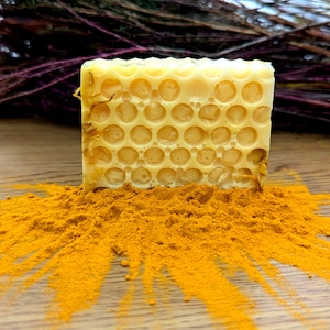 May include: A yellow honeycomb-shaped bar of soap sits on a pile of bright orange turmeric powder.