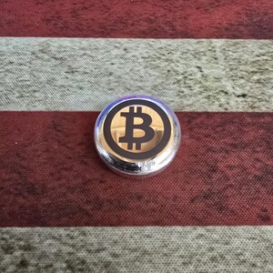 May include: A silver Bitcoin coin with a black Bitcoin symbol on a gold background. The coin is set against a red and white striped background.