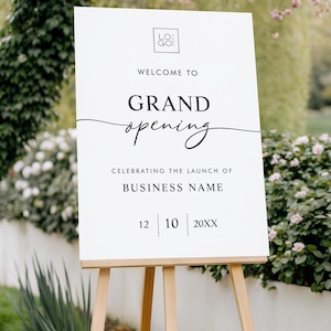 May include: A white sign on a wooden easel with the words "WELCOME TO GRAND opening" in black script. The sign also includes the text "CELEBRATING THE LAUNCH OF BUSINESS NAME" and a date. The background features greenery and a brick walkway.