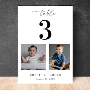 Peut inclure: Carte de numéro de table blanche avec le mot « table » en écriture cursive au-dessus d'un grand chiffre 3 noir. Deux photos de bébés sont en dessous, avec des noms et une date en bas.