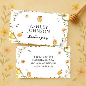 Può includere: Due biglietti da visita con un tema floreale e di api. La carta in alto recita "ASHLEY JOHNSON Apicoltrice". La carta in basso include un numero di telefono e un indirizzo email. Le carte sono decorate con illustrazioni ad acquerello di vasetti di miele, api e fiori.
