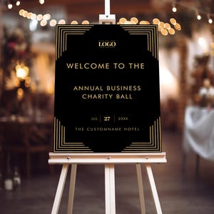 Könnte beinhalten: Ein schwarzes Schild auf einer weißen Staffelei mit goldenem Text, der lautet: "WILLKOMMEN ZUM JÄHRLICHEN BUSINESS CHARITY BALL" und das Datum "27. JULI 20XX". Das Schild hat einen goldenen Art-Deco-Rand und ein Logo oben.