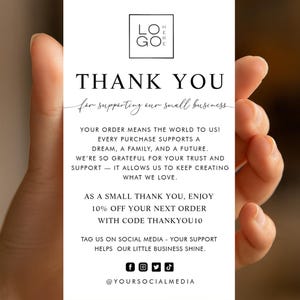May include: A white rectangular card held by a hand, with black text expressing thanks for supporting a small business. The card includes a logo, social media icons, and a discount code for the next order.
