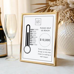 May include: A gold-framed sign with a fundraising thermometer graphic, aiming for £10,000. A champagne bottle and glass are in the background. The sign reads "Please Help Us Reach" and "Every contribution brings us one step closer to making a real impact."