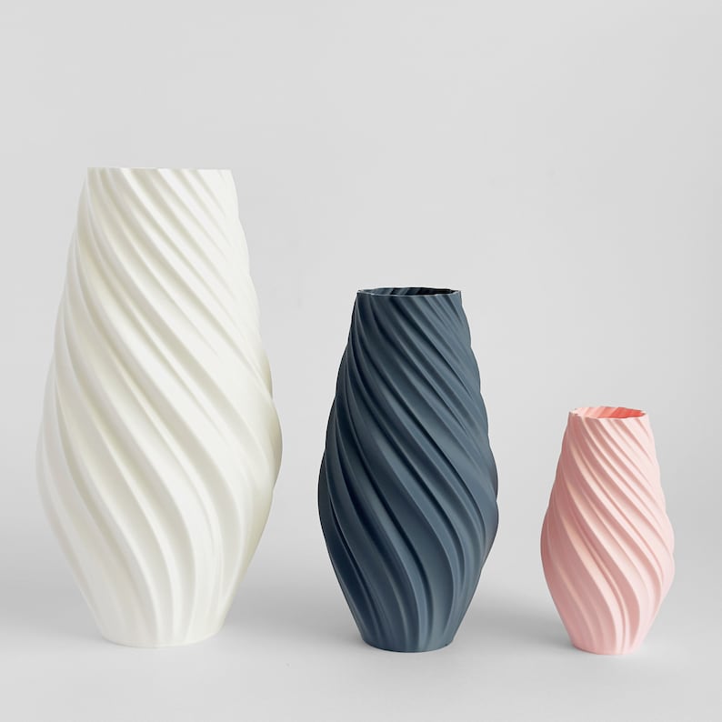 May include: Three ceramic vases with a swirling pattern. The largest vase is white, the middle vase is dark gray, and the smallest vase is light pink.