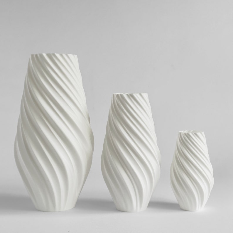 May include: Three white ceramic vases with a swirling, textured design. The vases are arranged in order of size, with the largest vase on the left and the smallest vase on the right.