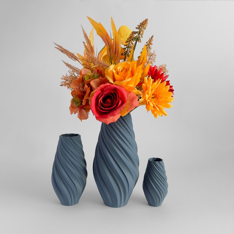 May include: Three blue ceramic vases with a swirling design. The largest vase holds a bouquet of orange, yellow, and red silk flowers.