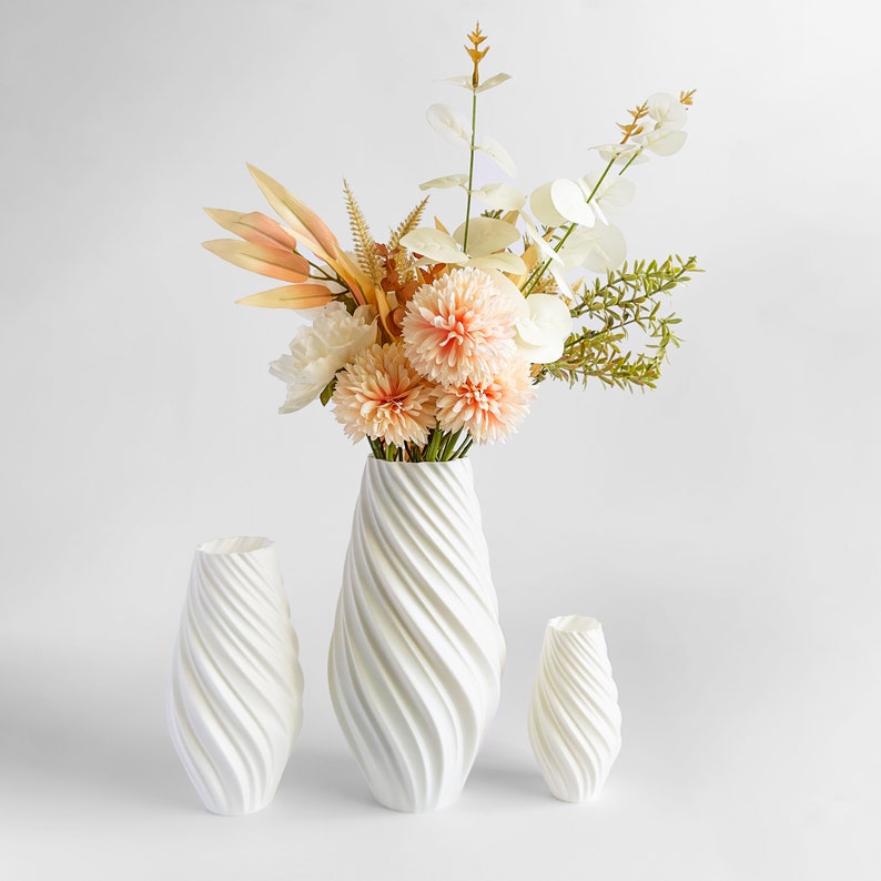 May include: Three white ceramic vases with a swirling design. The largest vase is filled with a bouquet of peach and white flowers.