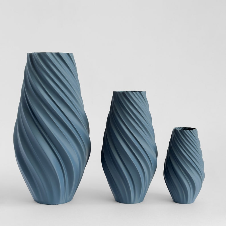 May include: Three blue ceramic vases with a swirling, textured design. The vases are arranged in order of size, with the largest vase on the left and the smallest vase on the right.