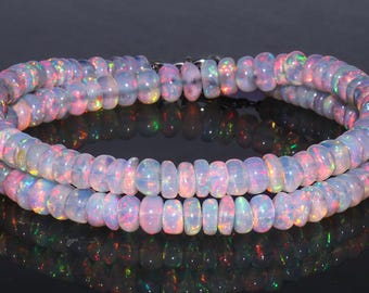 May include: Two strands of iridescent opal beads, showcasing a spectrum of colors including pink, blue, and green. The beads are strung together, creating a necklace or bracelet with a reflective surface.
