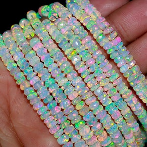 May include: Strands of faceted opal beads. The beads are primarily white with flashes of iridescent color, including pink, green, and yellow. The beads are strung together, creating a layered effect. The background is dark.