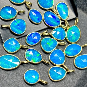 Könnte beinhalten: Eine Sammlung von 18 blauen Opal-Anhängern mit goldenen Fassungen. Die Opale sind facettiert und haben eine Vielzahl von irisierenden Farben.