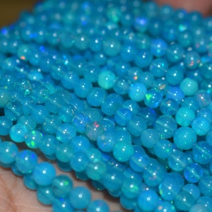 May include: Close-up of strands of round, light blue opal beads. The beads have a smooth, polished surface and a subtle iridescent sheen. The beads are approximately 4mm in diameter, perfect for jewelry making.