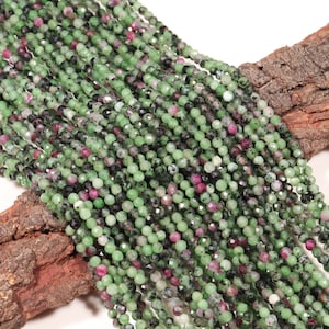 Peut inclure: Un brin de perles de pierres précieuses vertes et roses. Les perles sont rondes et facettées, et elles sont enfilées sur un fil transparent. Les perles sont disposées de manière aléatoire et elles ont toutes à peu près la même taille.