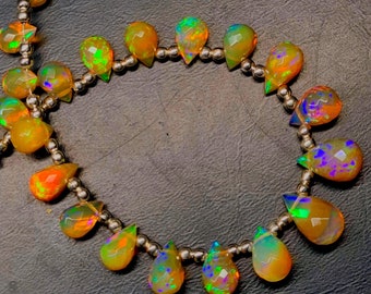 May include: A strand of iridescent opal gemstone beads in a teardrop shape. The beads are strung on a silver chain and are a mix of yellow, orange, and green.
