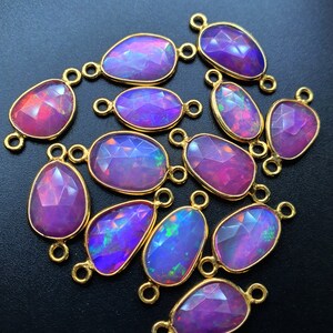 May include: A group of 14 purple and iridescent opal gemstone connector charms with gold-toned metal accents. The charms are oval-shaped and have a faceted finish.