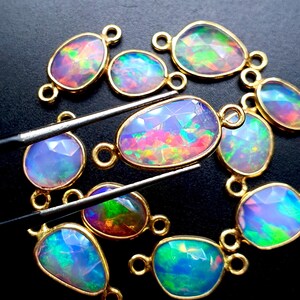 May include: A collection of 10 opal gemstone connector charms with gold-toned metal settings. The opals are iridescent with shades of blue, green, pink, and purple.
