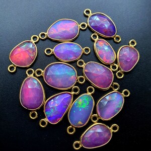 May include: A group of 15 iridescent opal gemstone connector charms with gold-tone metal loops. The opals are a mix of pink, purple, and blue.