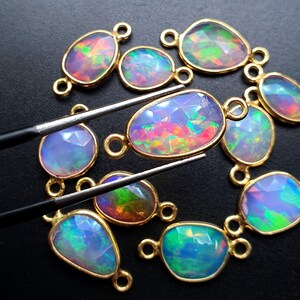 May include: A collection of 10 opal gemstone connector charms with gold-plated settings. The opals are iridescent with shades of blue, green, pink, and orange.