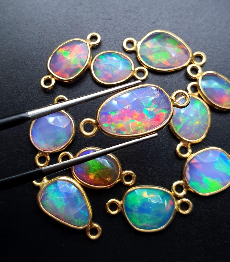 May include: A collection of 10 opal gemstone connector charms with gold-plated settings. The opals are iridescent with shades of blue, green, pink, and orange.