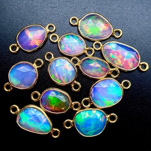 May include: A group of 12 iridescent opal gemstone connector charms with gold-toned metal accents. The opals are oval shaped and have a variety of colors, including blue, green, pink, and purple.