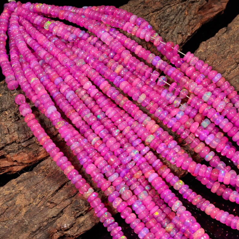 May include: A strand of pink opal beads, with a slight iridescent shimmer, arranged in rows on a wooden surface.