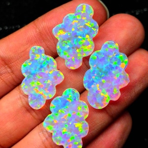 Pode incluir: Quatro cabochões em forma de nuvem com um jogo de cores vibrante, apresentando reflexos iridescentes de verde néon, amarelo brilhante e azul elétrico sobre uma base branca translúcida. Cada peça possui uma superfície lisa e polida.