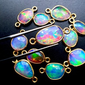 May include: A collection of 10 oval-shaped opal gemstone connector charms with gold-toned metal settings. The opals are iridescent with shades of blue, green, pink, and purple.