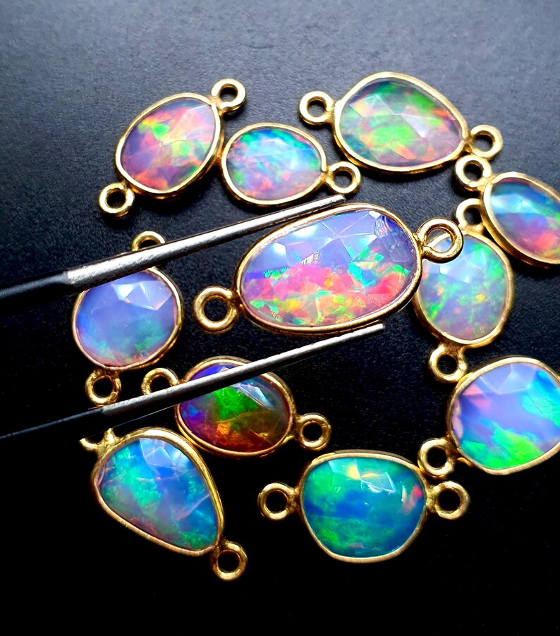 May include: A collection of 10 oval-shaped opal gemstone connector charms with gold-toned metal settings. The opals are iridescent with shades of blue, green, pink, and purple.
