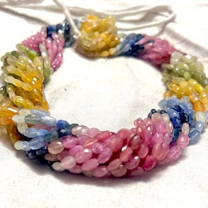 May include: A strand of colourful gemstone beads, featuring a mix of yellow, green, blue, and pink oval-shaped beads. The beads are strung on a white cord and are arranged in a circular pattern.
