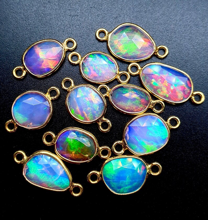 May include: A group of 12 iridescent opal gemstone connector charms with gold-toned metal accents. The opals are oval shaped and have a variety of colors, including blue, green, pink, and purple.