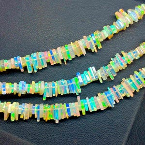 May include: A strand of iridescent opal beads, each bead is a rectangular prism with a slightly irregular shape. The beads are strung together to form a necklace.
