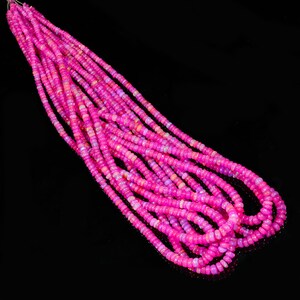 May include: A strand of pink opal beads, with a slight iridescent shimmer, arranged in a loose pile on a black background.