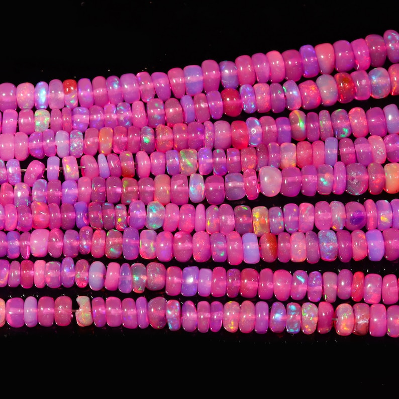 May include: A strand of pink opal beads, with a variety of shades and iridescent flashes. The beads are oval shaped and have a smooth, polished finish.