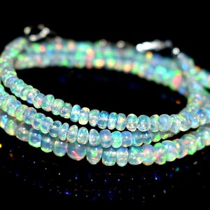 May include: A strand of iridescent opal beads, with a light blue and white color, is wrapped around itself in a circular shape. The beads are small and round, and they have a subtle shimmer to them.