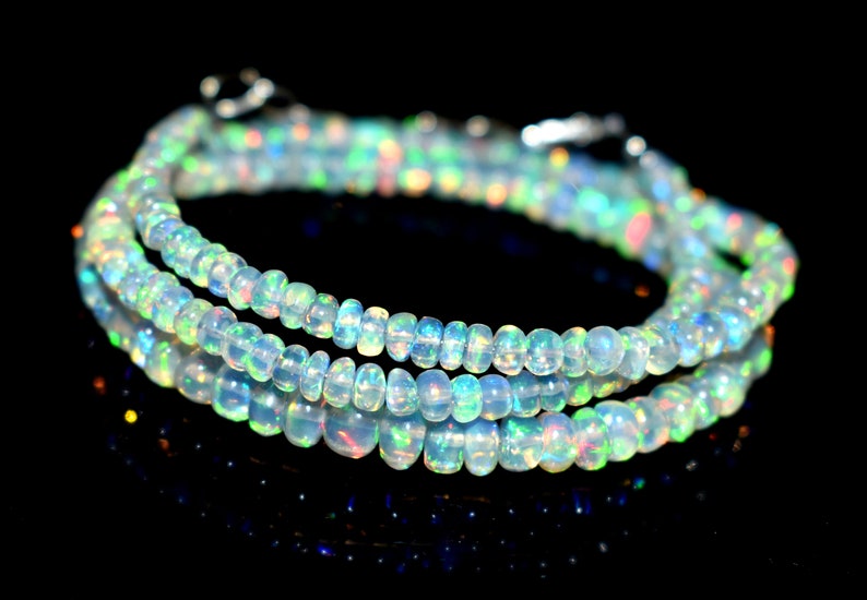 May include: A strand of iridescent opal beads, with a light blue and white color, is wrapped around itself in a circular shape. The beads are small and round, and they have a subtle shimmer to them.