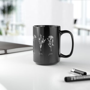 Puede incluir: Taza de cer&aacute;mica negra con un dise&ntilde;o floral blanco y los nombres "Flora", "Laura" y "Jesse" impresos en el lateral.